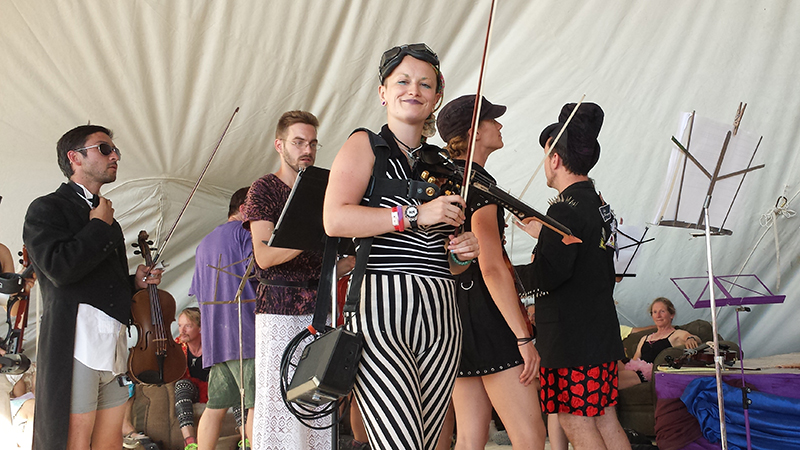 First chair Madelaine Ripley (black and white stripes) and other violinists with the PlayaPops Symphony prepare for their debut performance at Burning Man this year (2014