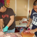 The men in the family cut up the pig in garage in preparation for the feast.