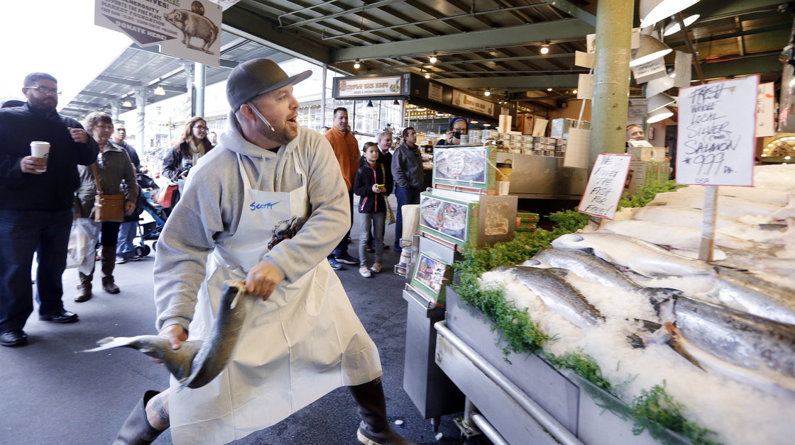 A fishmonger tosses a just-purchased fresh salmon to a colleague behind the counter at the Pike Place Fish Market in Seattle. Photo: Elaine Thompson/AP