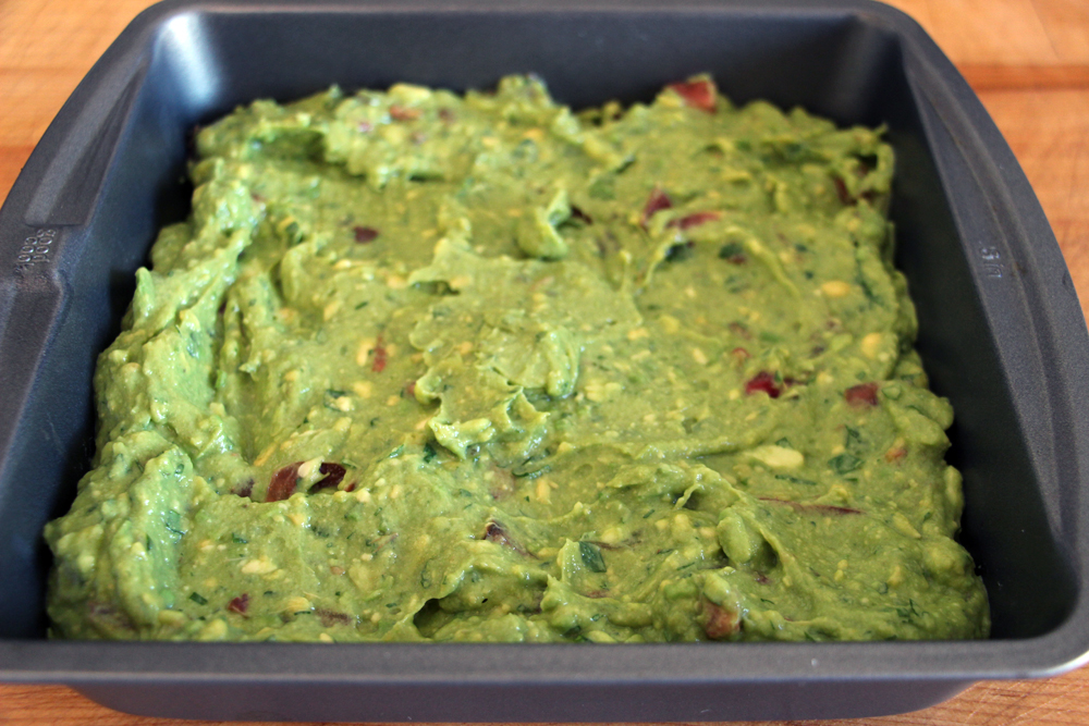 Spread the guacamole in a shallow 9-inch square or round serving or baking dish .