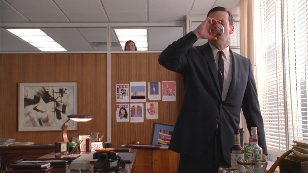 Don (Jon Hamm) downs a drink in the office, spied on by Peggy Olson (Elisabeth Moss.) (Photo: AMC) 