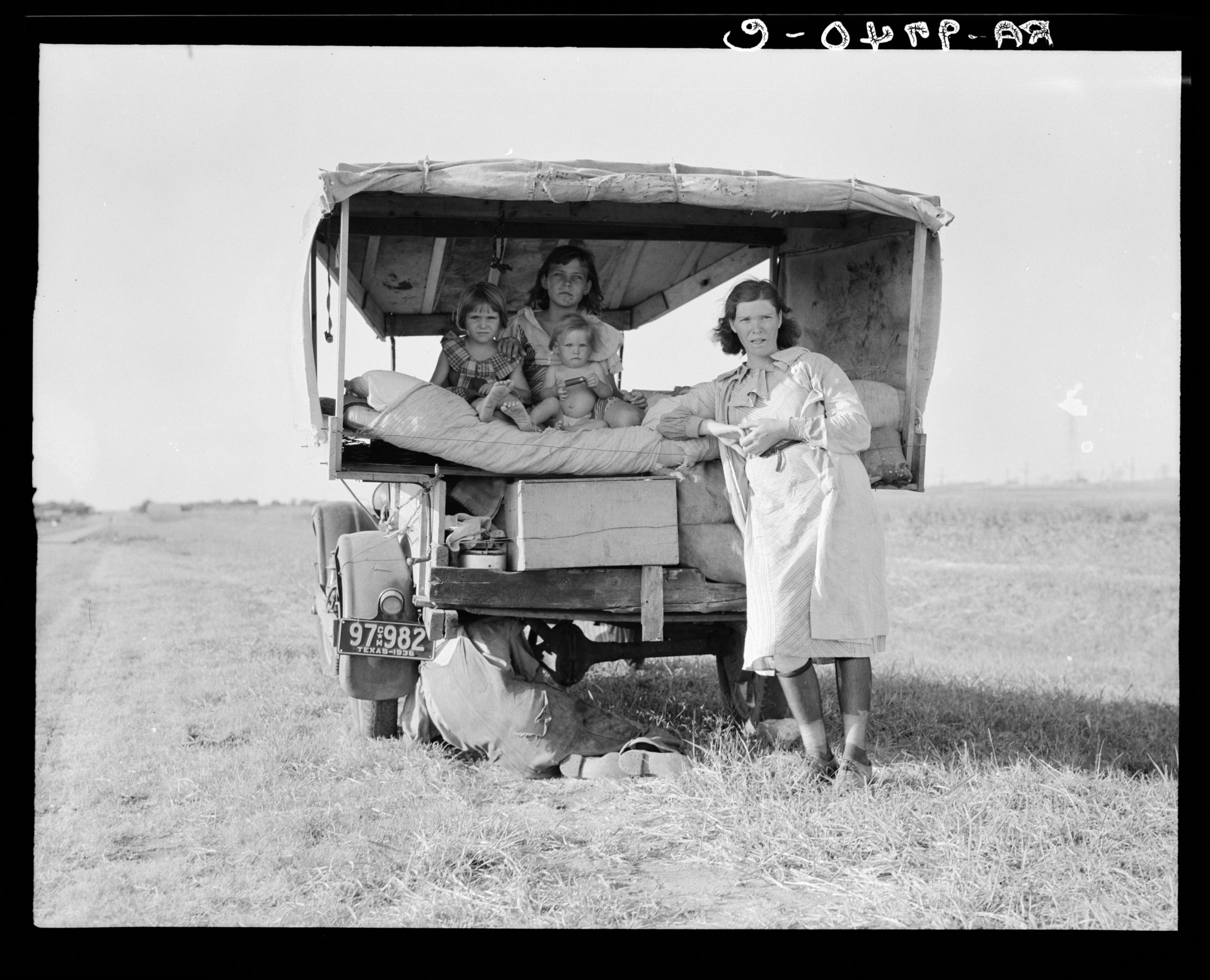 A family traveling between Dallas and Austin, Texas. "The people have left their home and connections in South Texas, and hope to reach the Arkansas Delta for work in the cotton fields," Lang wrote in her notes. "Penniless people. No food and three gallons of gas in the tank. The father is trying to repair a tire. Three children. Father says, 'It's tough but life's tough anyway you take it.' "