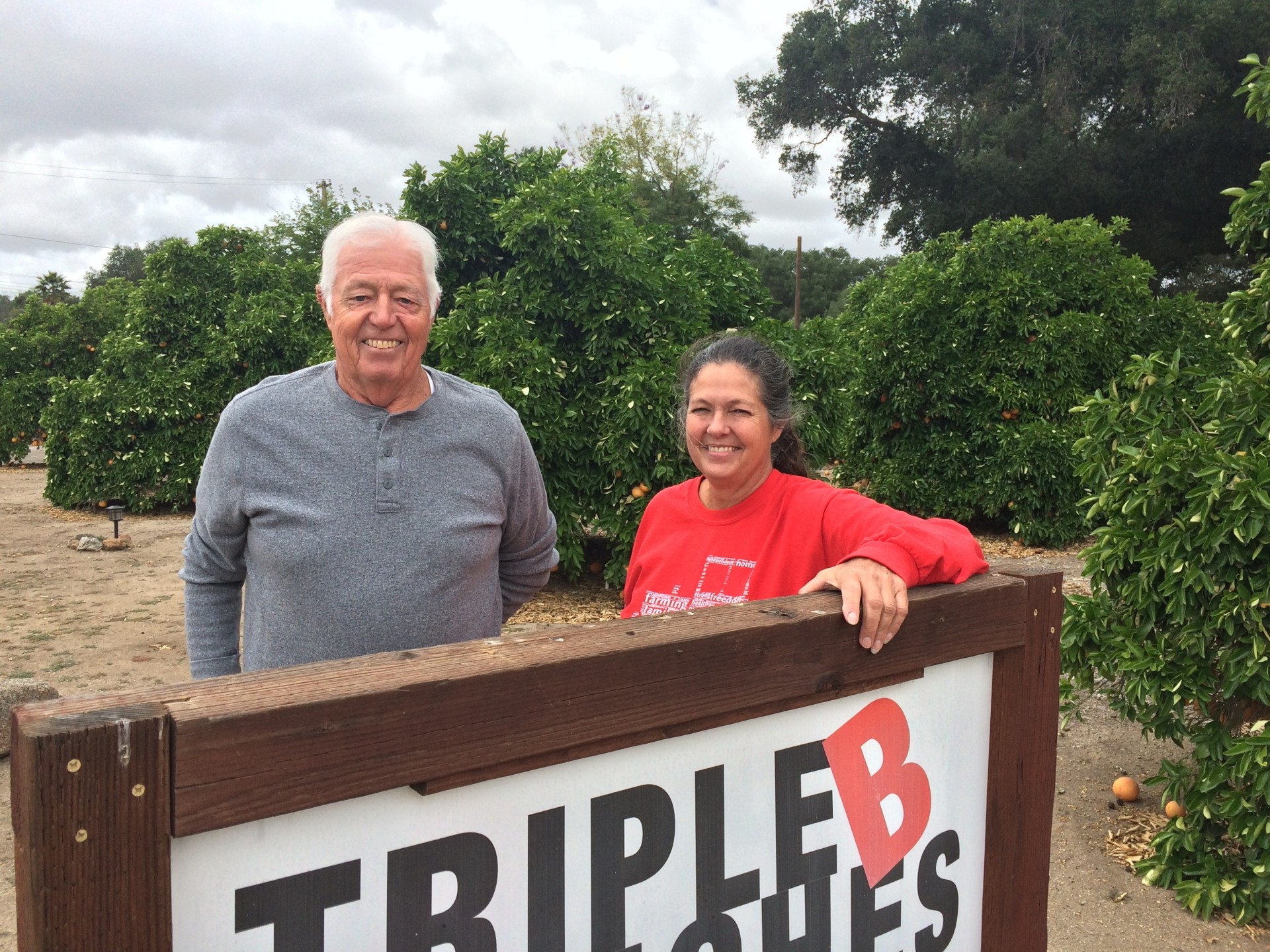 Gary Broomell and his daughter, Debbie, pose behind a sign on their ranch in San Diego County. Their family has been growing citrus for generations, but lately, it's been hard staying in the black growing oranges, so they started a vineyard a few years ago.