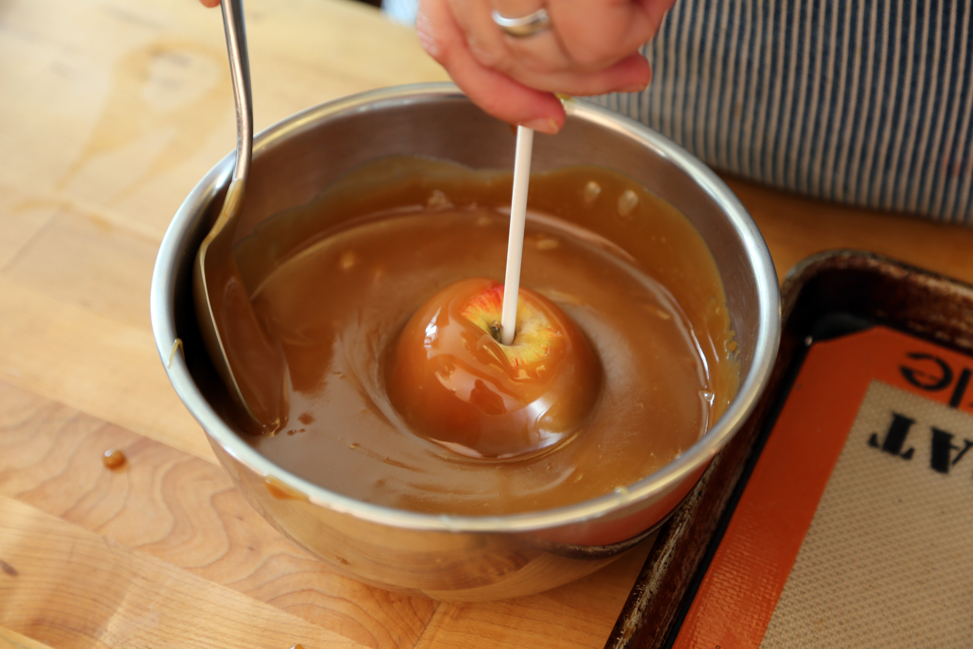 Grease the lined parchment or silicone. Holding the stick, dip each apple into the caramel.