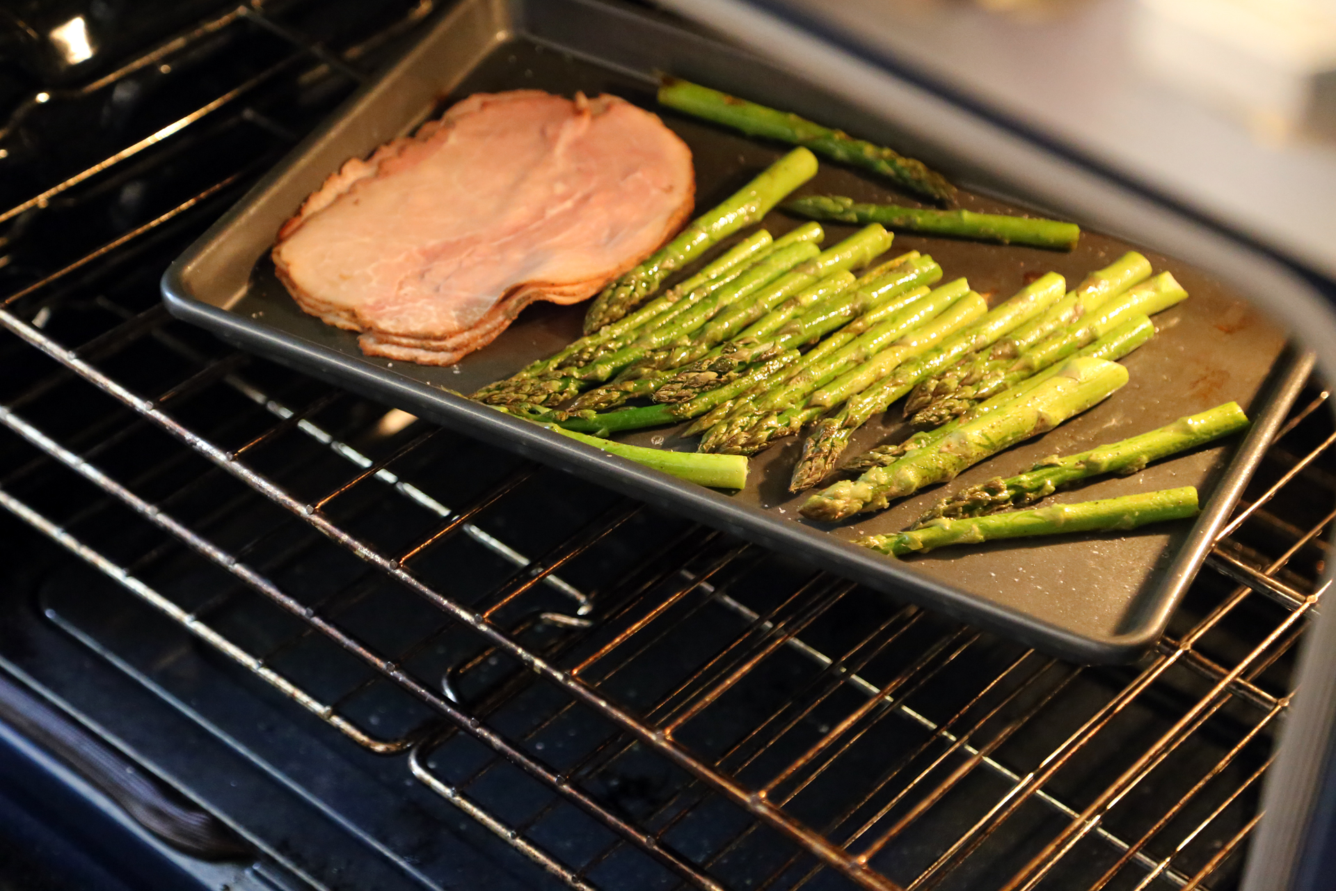 Just before the asparagus is ready, push it over to the side of the baking sheet, and add the ham slices, spreading them out.