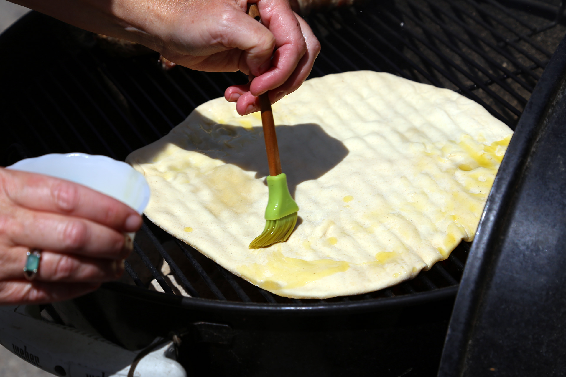 Lay the dough round on the grill, olive oil–side down. Brush the top of the dough lightly with olive oil.