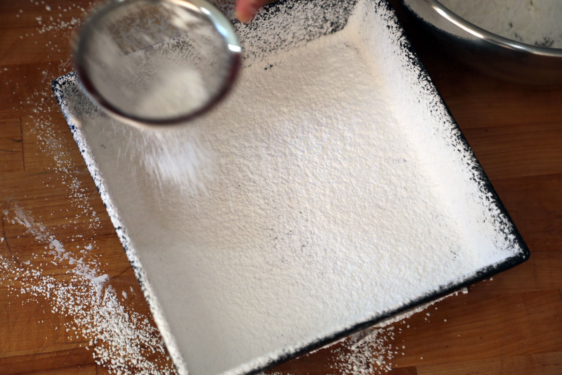 In a large bowl, sift together the powdered sugar and cornstarch. Using the sifter, dust the baking pan with about half of the mixture, making sure to cover the sides by tilting the pan to coat it evenly.