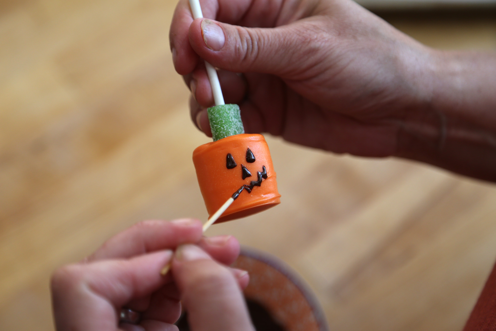 Using a toothpick, draw spooky eyes and a scary mouth onto the marshmallow pumpkins.