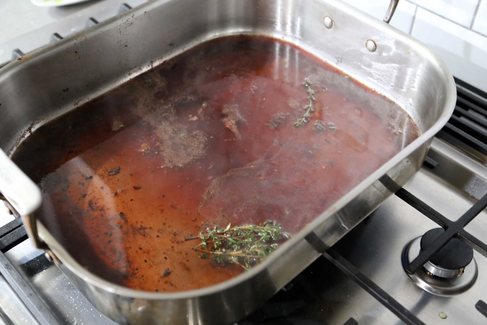 Return the juices to the roasting pan and set the pan on the stovetop over medium heat (you may need to put it over the griddle burner or 2 burners). Add the beef stock, wine, and thyme sprigs.