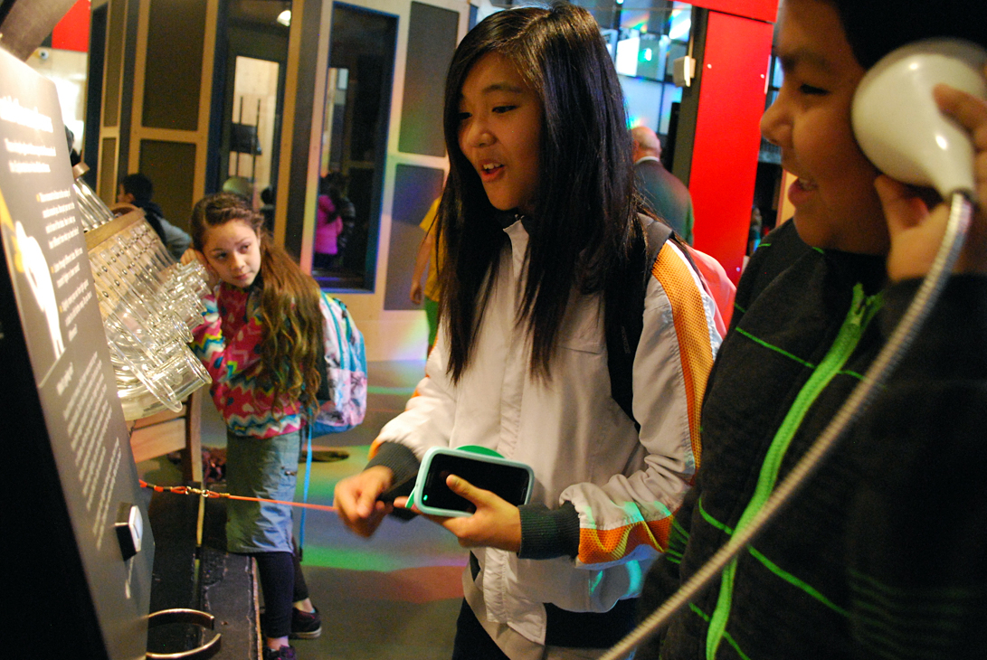 Jasmine Capili and Cesar Viallsenor try to figure out an Exploratorium exhibit on sound waves while their classmate, Stephanie Posadas Torres, listens at the end of a glass tube in the background. All three sixth-grade students are from Vallejo, Calif. 