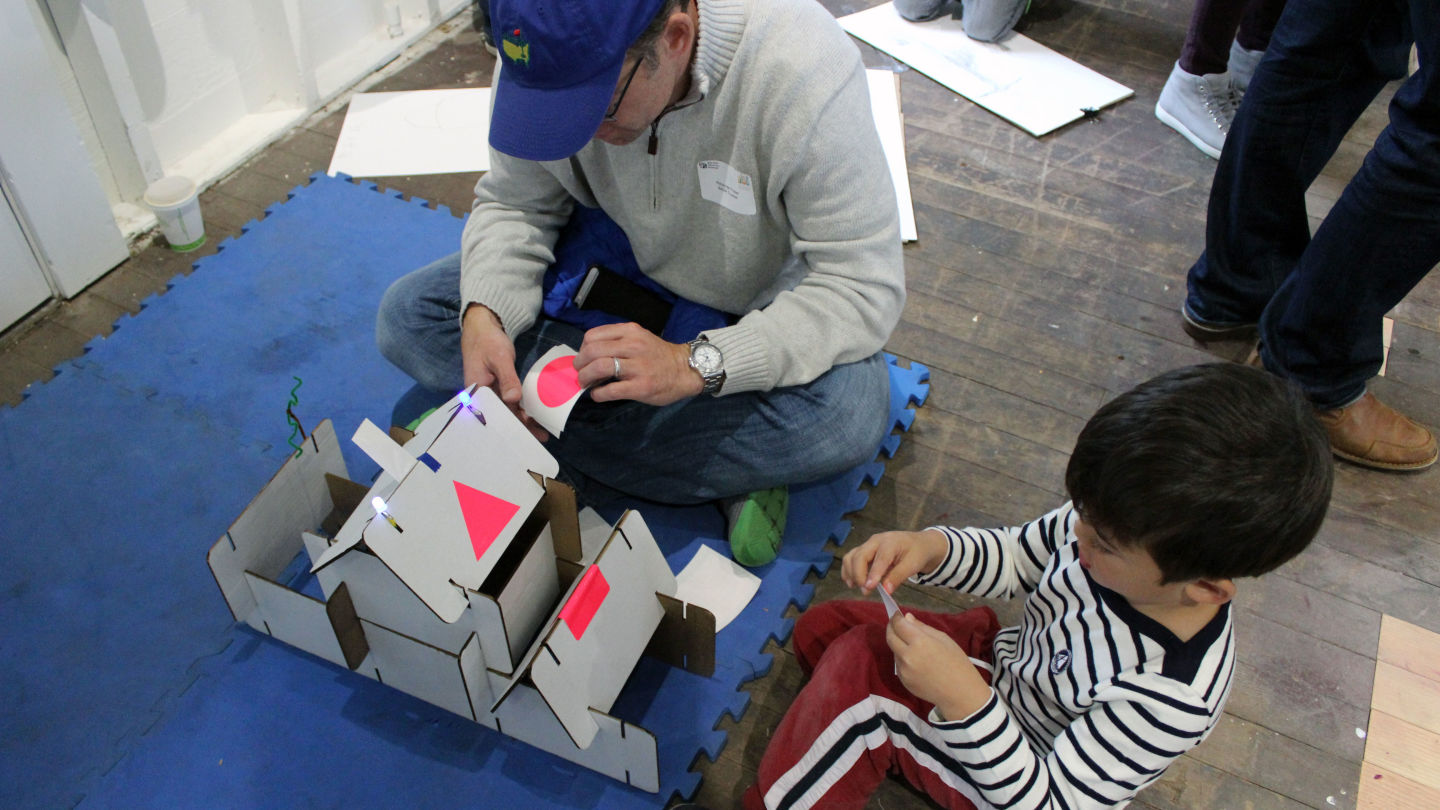 A dad and son beautify the building they built with pre-cut cardboard pieces.