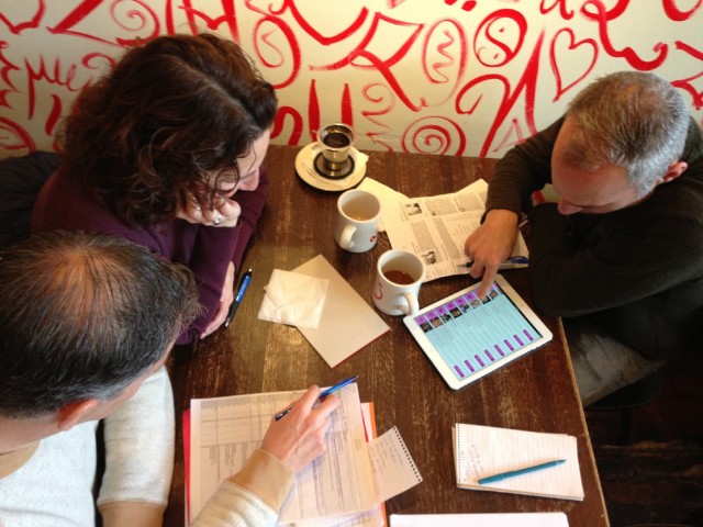Contestants Joel (left) and Jamie (right) join teammate Lisa at Ritual Café in San Francisco as they huddle over spreadsheets and data before making their 2014 Dead Pool picks. (Scott Shafer/KQED)