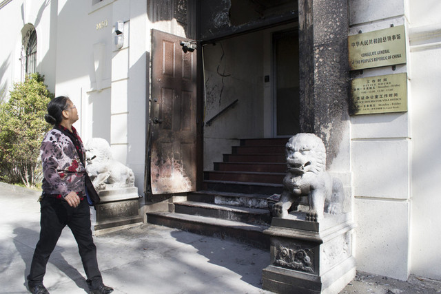 Xue Kui Zhang, who moved to San Francisco from China in 2008, walks past the entrance of the Chinese Consulate, which is charred after a suspected arson incident last night. (Sara Bloomberg/KQED)