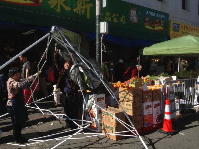 A merchant on Stockton Street tries to set up his stall, but gusts of wind make it a protracted struggle. (Patricia Yollin/KQED)