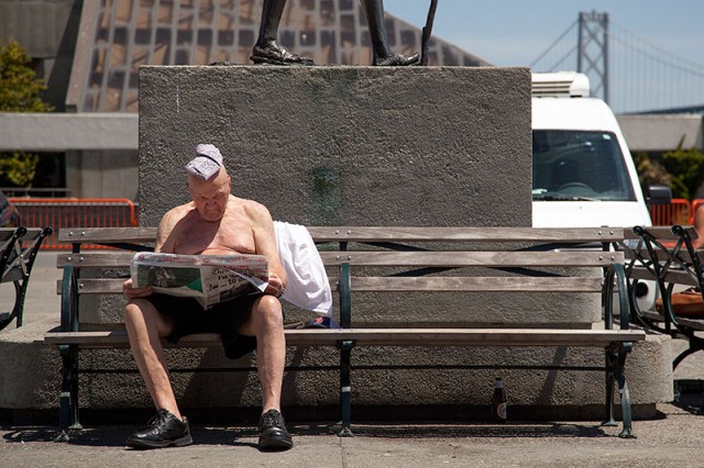 A man suns himself while reading the newspaper next to the Ferry Building (Mark Andrew Boyer/KQED)