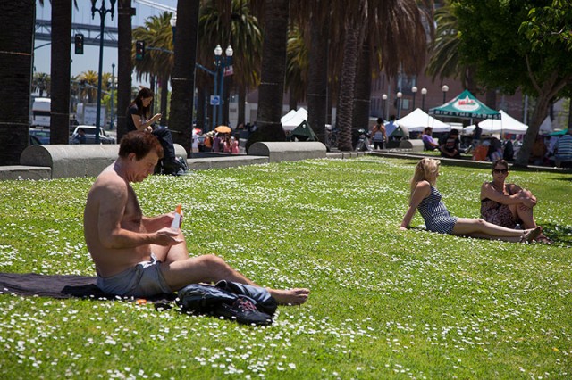 Dirk Wyse applies sunscreen while lounging on the grass along the Embarcadero (Mark Andrew Boyer/KQED)