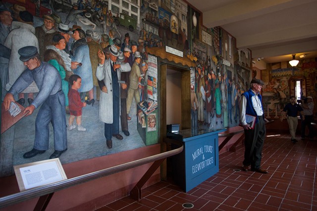 Michael Gorden, a docent for San Francisco City Guides, stands in front of one of Coit Tower's murals (Mark Andrew Boyer / KQED)