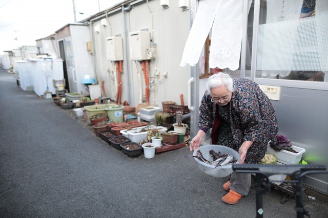 An elderly woman holds a container filled with fish given by her neighbor outside her temporary house. (Yuriko Nakao/Getty Images)