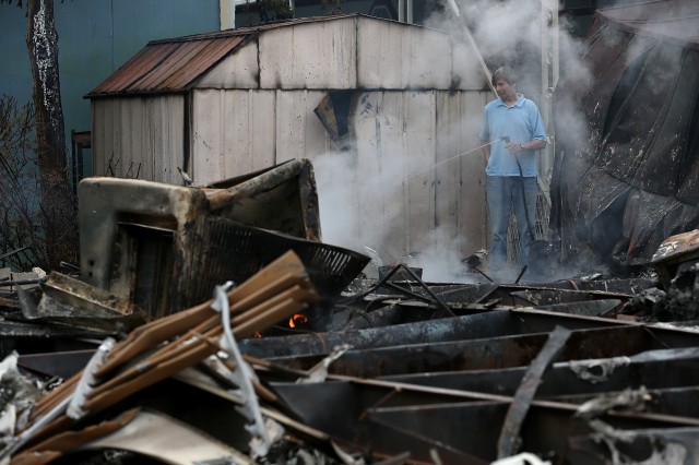A man uses a garden hose cool hot spots from a fire at a mobile home park. (Justin Sullivan/Getty Images)