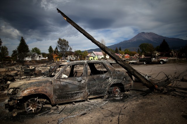 A burned utility pole rests on a burned-out car that sits among the remains of a destroyed home in Weed, California. (Justin Sullivan/Getty Images)