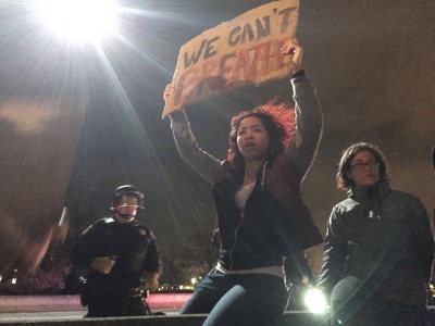 A woman holding a sign in reference to Eric Garner is about to be shoved off a dividing wall on Interstate 880 in Oakland on Dec. 5. (Alex Emslie/KQED)