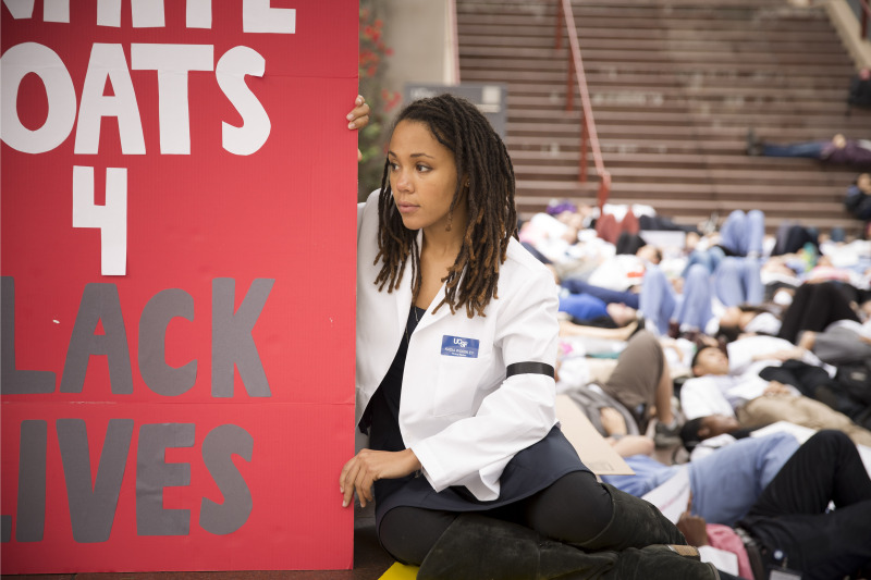 Kadia Wormley, a UCSF medical student, wears a black arm band in solidarity with the families of Michael Brown and Eric Garner. The sign says "white coats 4 black lives." 