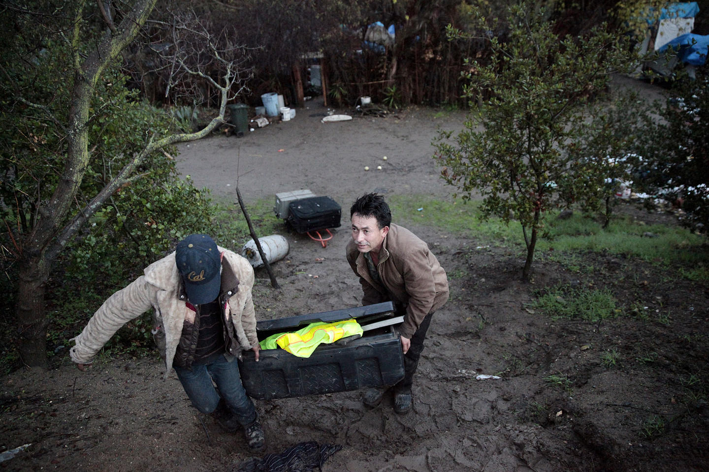 Jose Alcala, right, removes his belongings after living at The Jungle for two years. Rain and mud has complicated the move for many residents. (James Tensuan/KQED) 