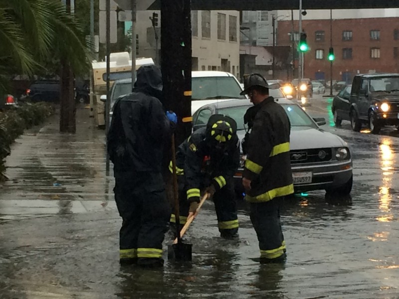 S.F. Firefighters work to clear a storm drain at 14th St. and Harrison St. in San Francisco ,Thursday morning. (Julia McEvoy/KQED)