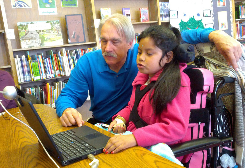 Chris Beatty, assistive technology professional for Oakland's schools, shows Jacquelyn Funes how to operate a laptop with a sensor mounted on her forehead.