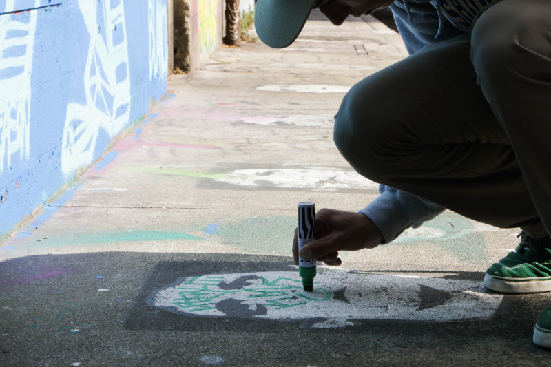 A graffiti writer tags on top of a piece of street art. (Jeremy Raff/KQED)