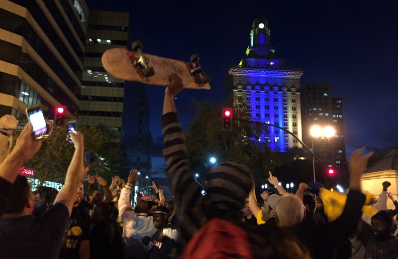 Fans celebrate the Warriors victory in front of Oakland City Hall, which is lit up in Warriors blue and yellow. (Adam Grossberg/KQED)