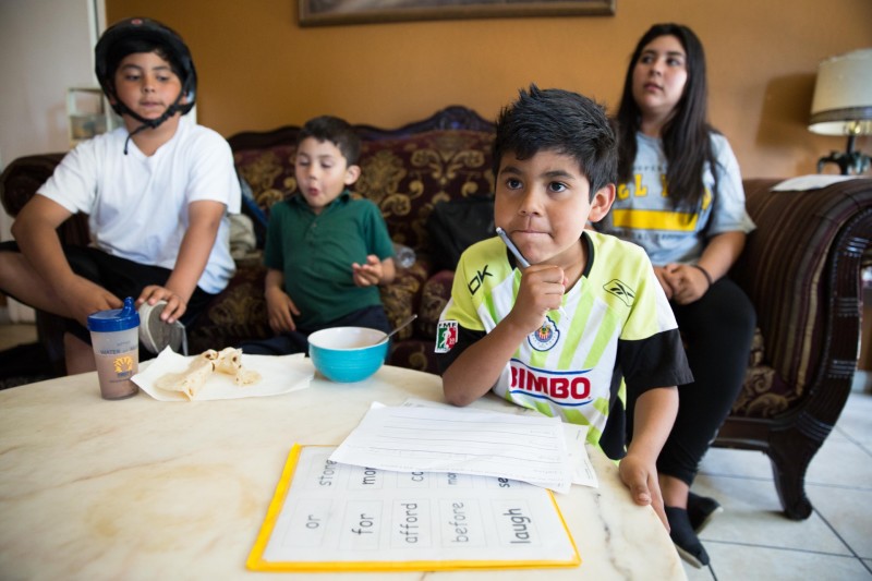 Bryan Luque, seven, works on his English homework, with siblings Angel, Valentin and Lidia behind.
