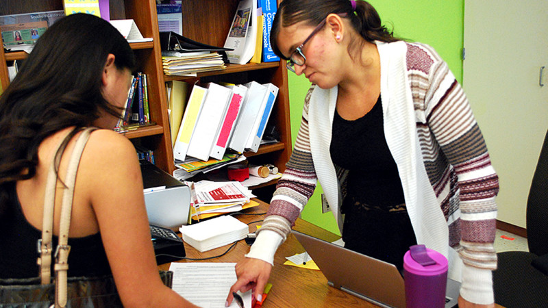 Reyna Valenzuela, standing, waits on hold for one Bell High School student while answering a question for another. Valenzuela is a member of the Southern California College Advising Corps based in Los Angeles.