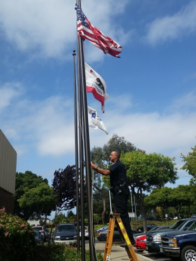 A Hayward police officer lowers a flag at the department to half-staff Wednesday after the fatal shooting of Sgt. Scott Lunger.