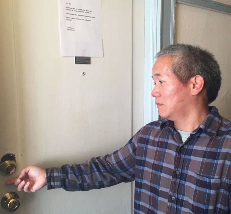 Hotel Astoria resident Owen Wang shows his damaged door. A note above says management has changed the lock.