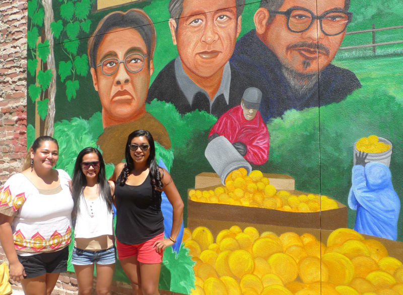 Angelica Perez, Melanie Retuda and Larissa Portillo (L-R) in front of a recently-completed mural in downtown Delano featuring Philip Vera Cruz, Cesar Chavez and Larry Itliong.