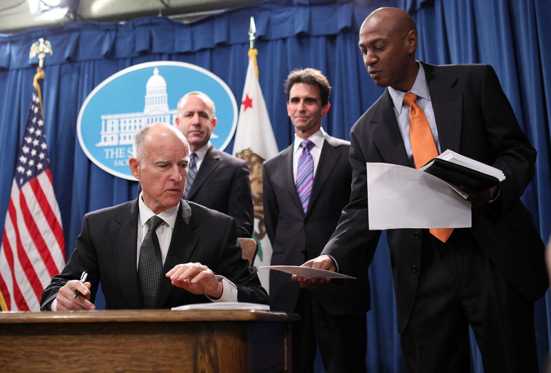 Gareth Elliott (R) hands Gov. Jerry Brown paperwork during a bill signing on March 24, 2011. A powerful lobbying firm announced Elliott would be joining their team just days after Elliott left the Brown administration.