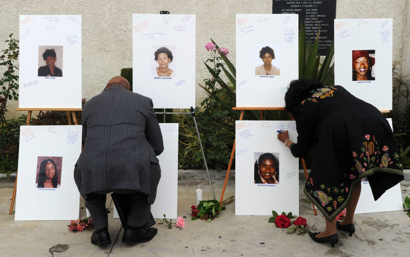 Reverend Dr. Kelvin Calloway (L) leaves a message on photographs set up as a memorial for 10 of the victims of the serial killer dubbed the Grim Sleeper.