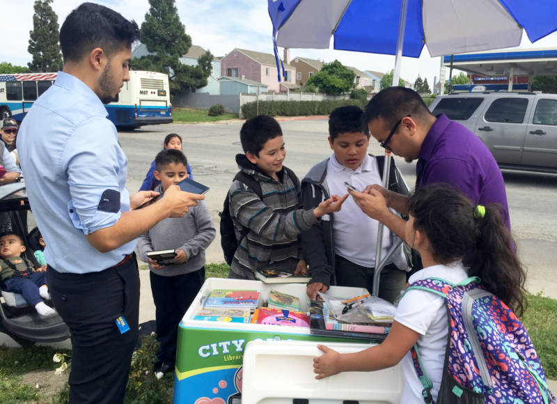 Librarian Luis Alejandre (R) and Library Clerk Luis Moya (L) help kids check out books from the Paletero cart.