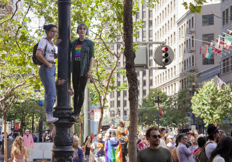 Two friends hang from a light post in order to get a better view of the parade.