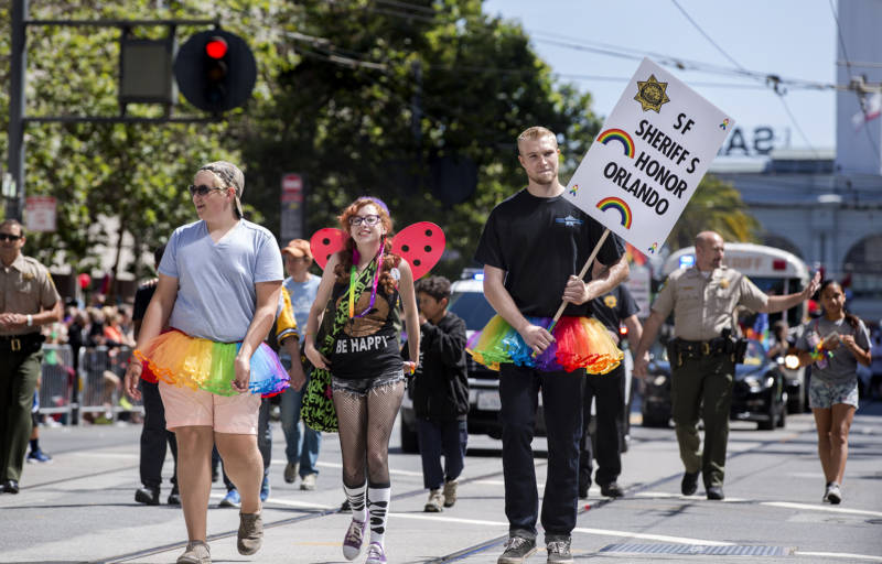 A man holding a sign supporting Pride on behalf of the SF Sheriff's Department marches down Market Street.