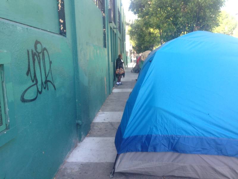 Angela Clifton-Flax stands in the distance outside her tent on Shotwell in the Mission. She said people need housing not shelters.