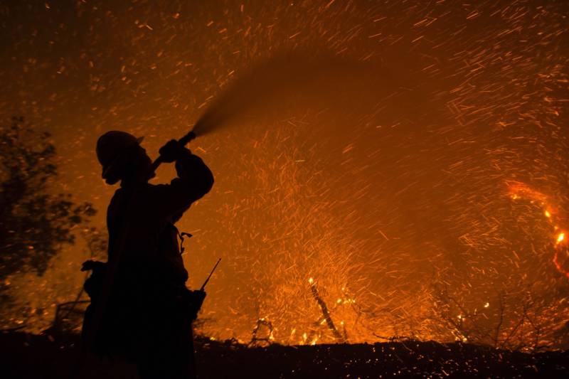 Embers fly around a firefighter with a hose, June 17 at the Sherpa Fire near Santa Barbara.