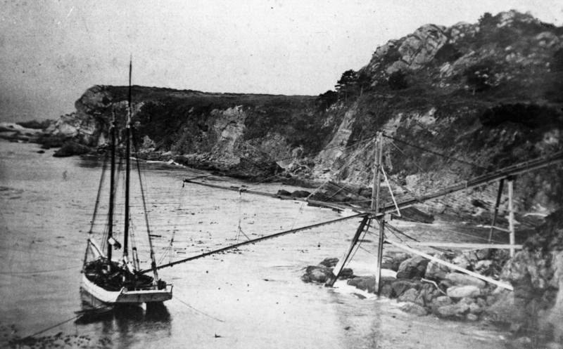 A waiting schooner at a Timber Cove doghole port is moored at three points, perilously close to shore, to receive its cargo.