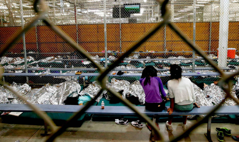 Two young girls watch television from their holding area where hundreds of mostly Central American immigrant children were being processed and held at the U.S. Customs and Border Protection Nogales Placement Center in June, 2014.