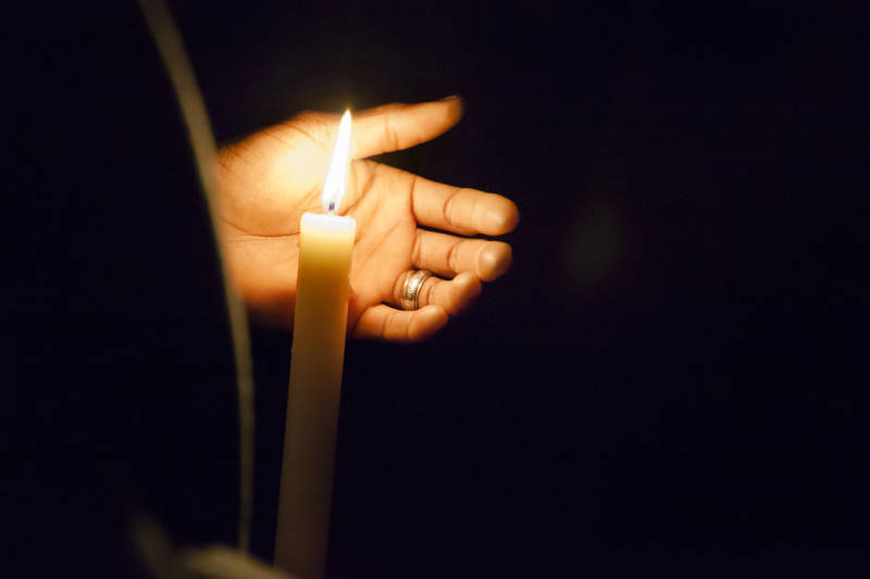 A mourner protects a candle-flame from the elements during a candle light vigil at Lake Merritt on December 5, 2016.