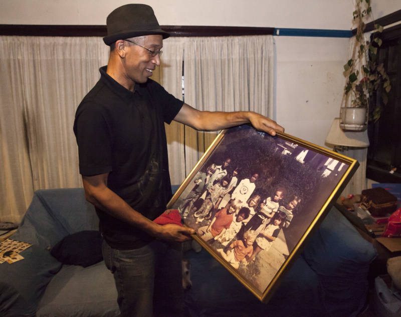 Musashi “Moose” Lethridge holds a family photo of himself (top center) and his sister (bottom center) as children along with several other friends who grew up in their neighborhood in Oakland.