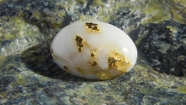 A small cabochon of gold quartz rests on serpentinite
