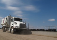 A feed truck drives along a concrete bunk in a cattle feedlot.