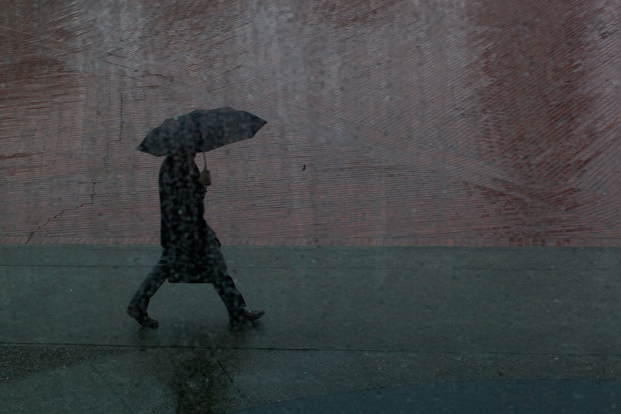 A pedestrian with an umbrella walks in the rain in front of San Francsico's Embarcadero Center. (Mark Andrew Boyer / KQED)